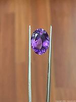 Front view of oval purple amethyst held in tweezers