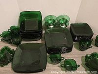 Grouped view of all green pressed glass pieces: stacks of square plates, cups, dessert bowls and wavy dish
