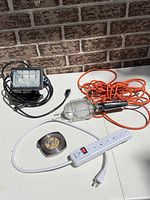 All items laid out: halogen work light, trouble light with orange cord, power strip, metal case tape