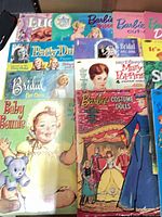 Front view showing multiple paper doll cut-out books including Baby Bonnie, Bridal Cut-Outs, Barbie Costume Dolls