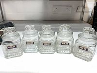 Front view of five Koeze glass canisters lined up