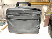 Front view of black nylon laptop bag showing exterior zip pocket and top handle