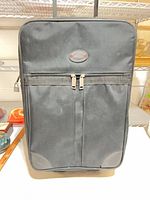 Front view of black soft-sided suitcase showing badge, front pocket and overall condition