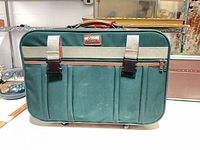 Front view of teal Skyway suitcase with straps, logo patch and wheels visible