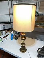 Full view of brass table lamp lit with shade on tabletop