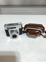 Front view of Zeiss Ikon Tenax camera beside brown leather case