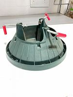 Top side view of green plastic Christmas tree stand showing red-handled screws