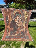 Full view of woven Madonna and Child tapestry hung outdoors showing design, colors, and fringed edges