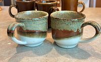 front view of two drip-glaze mugs with rest of lot behind