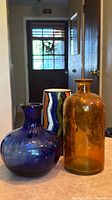 Front view of three glass vases: blue bulbous, multicolour zigzag, amber bottle