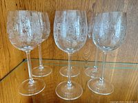 Front view of six matching floral etched wine glasses on shelf