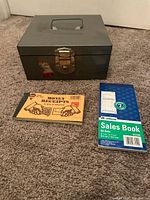 Front view of metal cash box, Adams sales book and money receipts pad