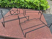 Four black metal planter holders on red mat, showing overall designs