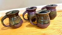 Set of four plum and green glazed stoneware mugs with black sip lids displayed side by side