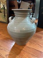 Full view of pale aqua blue pottery urn vase on wood floor
