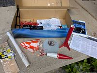 All components of the Estes rocket launch set displayed on surface: rocket parts, launch pad, rod, parachute, wires, instructions.