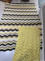 Both afghans displayed together; yellow openwork folded over multicolour chevron for size and colour comparison