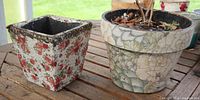 Square red rose floral planter and round pastel floral planter side by side on wooden surface