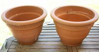 Two terracotta planters side by side on table, showing exterior form and rim motif
