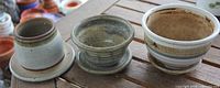 Front view of three ceramic pots showing glaze styles and attached saucers