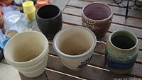 Five assorted ceramic pots displayed upright on wooden surface