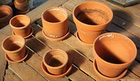 Six terracotta pots with saucers on wooden table, top view