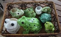 All eight ceramic frog pieces arranged inside wicker basket