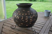 Front view of carved black clay vase on stand showing motifs and form