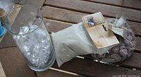Glass vase filled with clear gems beside bag of white sand and mesh bag of purple stones