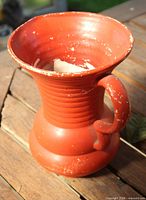front view of terracotta-orange pottery watering pitcher showing handle and rim wear