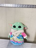 Front view of Grogu plush with measuring tape for scale