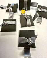 Front view of six sterling silver pendants on foam pads with grey ribbons