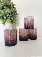 Four amethyst lowball tumblers stacked beside plant