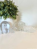 Group view of four clear glass animal figurines: owl, baby elephant, large elephant, rhino