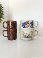 Two brown textured mugs stacked beside two beige floral mugs