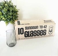 sealed cardboard box showing product name and capacity beside one glass