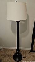 Full view of black metal floor lamp with white drum shade