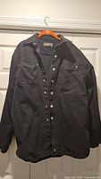 Front view of black Jesse James heavy cotton button-up shirt on hanger