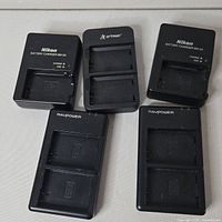 Five camera battery chargers laid out, showing brands and slots