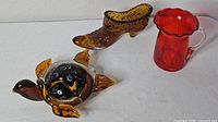 Overview of three glass pieces: turtle, shoe, red pitcher