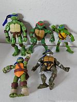Front view of all five TMNT figures standing and lying, showing sizes and bandana colours