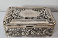 Closed jewelry box angled view showing raised floral motif and blank cartouche