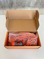 Open cardboard box showing coiled orange leash in clear zip bag and grey/red dispenser