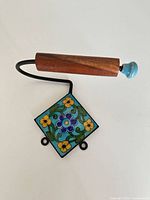 Full view of toilet paper holder showing wood spindle, blue knob, metal arm and floral tile backplate