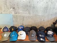 Full lineup of 13 baseball caps on table