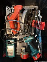 Overview of bin containing Makita drill, charger, batteries, circular saw, jigsaw, wrench set