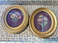 Two circular gold frames containing floral needlepoint on burgundy background