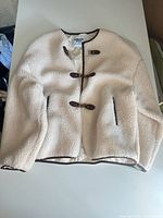 Front view of cream faux shearling jacket showing brown trim, toggle closures, and pockets