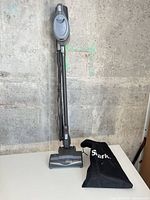 Full view of Shark Rocket stick vacuum standing upright next to accessory bag