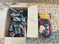 Box containing chrome sockets, driver handle, extension, folding multitool, next to sealed package of assorted bungee cords